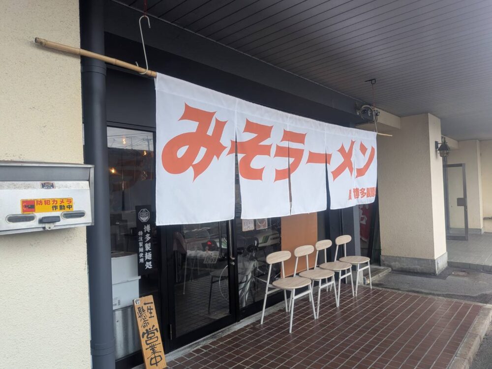 白地に「みそらーめん」と書かれたオレンジ色ののれんが目印の「みそらーめん専門店 みつぐ」の外観